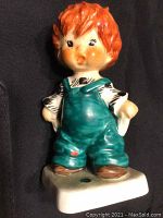 Front view of the Hummel figurine showing the boy with orange hair in teal overalls on the white base.
