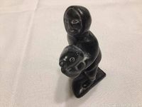 Front angled view of the dark stone carved indigenous figurine holding an animal head, showing detailed facial features and base.