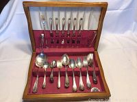 Full view of flatware set in wooden box with red velvet lining showing knives, forks, spoons, tongs.