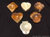 Six onyx ashtrays in varying shapes and colors placed on black cloth showing overall lot condition and shape variety