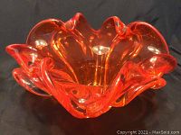 Top and angled view of the vibrant orange blown glass bowl with ruffled edges on a black background.