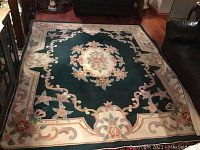 Photo showing the full Chinese handmade rug with floral medallion in the center and decorative cream border, placed on wooden floor between black leather furniture.