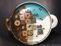 Full view of round ceramic platter with turquoise, brown, and white glazing showing floral decorations and dual handles.