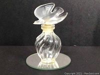 Front view of clear glass perfume bottle with swirl design and frosted dove stopper on a round mirror.