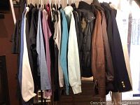 Overview photo showing a variety of women's clothing items hanging on a rack, mostly jackets, hoodies, and tops in various muted colors.