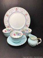 Full set photo showing one teacup and saucer, three small floral sugar bowls, pastel blue creamer, and Royal Doulton plate in background