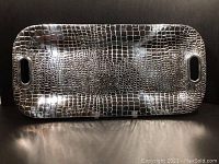 Front view of rectangular metal tray with crocodile pattern and cutout handles.