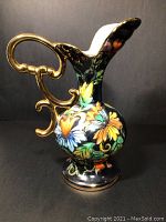 Front angle view of the vintage majolica pitcher showing colorful floral etching and ornate handle with gold trimming.