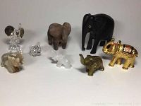 Nine miniature elephant figurines arranged on a flat surface showing variety of materials and sizes.