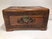 Front view of hand-carved camphor wood chest showing floral border carvings and brass latch.
