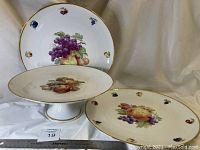 Full view of the three large round fruit platters, showing one footed platter and two flat platters with fruit and gold rim decoration.