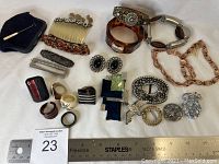 Overview of the vintage and antique costume jewelry lot showing bracelets, rings, hair accessories, brooches, clip-on earrings, and hooks with measuring rulers for scale.