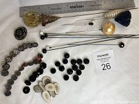 Full overview of assorted antique hat pins and buttons including glass, metal, and antler material with a ruler for scale