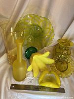 Overview showing 7 yellow art glass pieces including vases, bowls, a platter, and a small green piece. Pieces vary in shape and finish - some frosted, some clear swirl design.