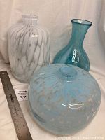 Three art glass vases together showing size relation and colors: white-blue tones with varied shapes.