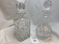 Two crystal decanters side by side, one square and one globe shape with stoppers, showing the overall appearance and design.