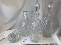 Three glass decanters together, two matching cut crystal with stoppers, one clear glass decanter, extra stopper to the side