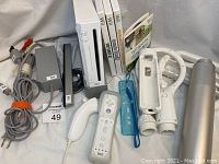Photo showing the Nintendo Wii console, power and AV cables, two Wii Remotes with wrist straps, Nunchuk controller, and assorted sports accessories including tennis racket, baseball bat, and steering wheel.