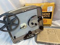 Front right perspective showing the Kodak Brownie 500 projector, its single reel, and the original box in the background.