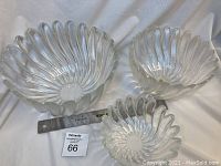 Three clear iridescent glass bowls nested together displayed on a satin fabric.