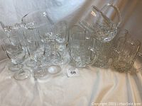 Set of clear crystal wine glasses and heavy glass beer steins arranged on white cloth.