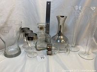 Full view of all glassware items including decanters, glasses, vase, and champagne flutes arranged on white background with measurement ruler