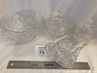 Large footed crystal pinwheel bowl, lidded footed covered bowl, cream pitcher with underplate, and lidded sugar bowl arranged on white cloth with ruler for size reference