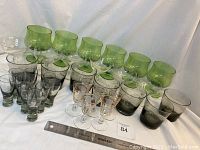 Full lot overview showing multiple glassware items with varying colors including smoke-colored, emerald green, and clear with gold detailing.