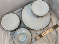 Photo showing stacks of dinner plates, side plates, fruit/sauce bowls, and one teacup with saucer all with silver trim on white porcelain.