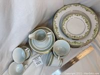 Photo showing multiple teacups, creamer, side plates and their decorative pattern with green and gold accents.