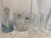 Overview of decanter, ice bucket and six flutes on white backdrop