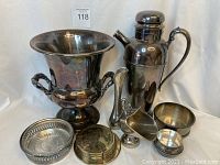 Overview of the silver plate items arranged together showing large ice bucket, coffee decanter, swan vase, coasters, trinket bowl, and sugar bowl.