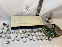 Wide shot showing collector thimbles lined up in front of rectangular decorative box, marbles container and small lamp.