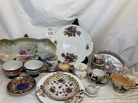 Photo showing assorted china pieces including floral platters, teacups, cream & sugar sets, and hand painted small containers