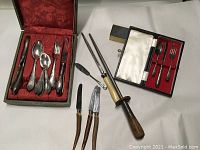 Full lot showing boxed silverware set, Birks children's tableware set, hand sharpener with wooden handle, and three horn-handled steak cutters