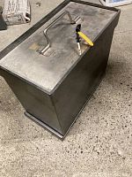 Side angle view of the heavy metal safe showing the textured body and stainless steel top with handle and keys inserted in the lock.