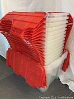 Stacked plastic crates with clear bodies and red flip lids showing lot contents.