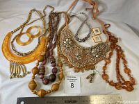 Full view of all included costume jewelry pieces laid on white cloth including necklaces and earrings with some beads and amber colored plastic elements.