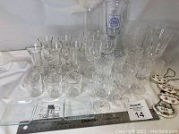 Overview of glassware including shot glasses, cut crystal wine glasses, tumblers, and tall glasses along with bottle labels laid out on white surface with a ruler for scale.