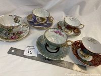 Full set of five Japanese teacups and saucers arranged with ruler for size reference showing various colors and designs.