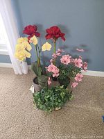 Photo showing five artificial floral decor pieces: two tall red amaryllis, one yellow orchid, one pink daisy arrangement, and one ivy plant.