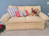 Front view of Ethan Allen wheat-coloured loveseat with three decorative pillows placed on it.