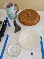 Photo showing antique Majolica pitcher, ceramic pumpkin-shaped covered pie dish, iron trivet, and 3 ceramic plates in a group.