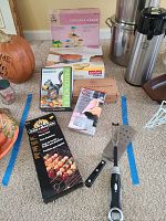 Overview of various baking and grilling items placed on carpet, including boxed cupcake stand, nutcracker, decorating tips set, cake slicer, and grilling tools.
