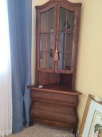 Front view of the oak reproduction corner cabinet with closed glass doors and three drawers below.