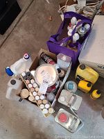 Overview of box and purple tote bag containing multiple paint-related products including bottles, cans, and spray cans placed on floor.