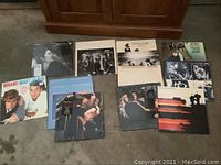 Thirteen vinyl rock LP albums spread on carpet floor showing various classic rock bands including Fleetwood Mac, Rolling Stones, Wham, Queen, and others.