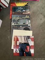 View of 10 rock and pop LP vinyl records stacked on floor, showing partially visible album covers including Bruce Springsteen's Born in the U.S.A., Billy Joel Greatest Hits, Paul Simon Graceland, Jim Croce, Al Green, John Oates Rock 'N Soul Part 1, Dr. Hook and others.