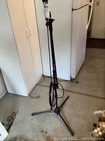 Digital Reference DR-VX1 microphone attached to black metal adjustable tripod stand with cord wrapped at base. Visible garage floor and cabinets in background.