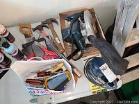 Photo showing various hand tools including hammers, saws, Ryobi finishing sander, and Black & Decker circular saw on a table.